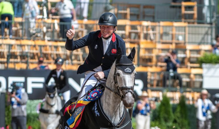 Man waiving on gray horse after winning eventing competition.